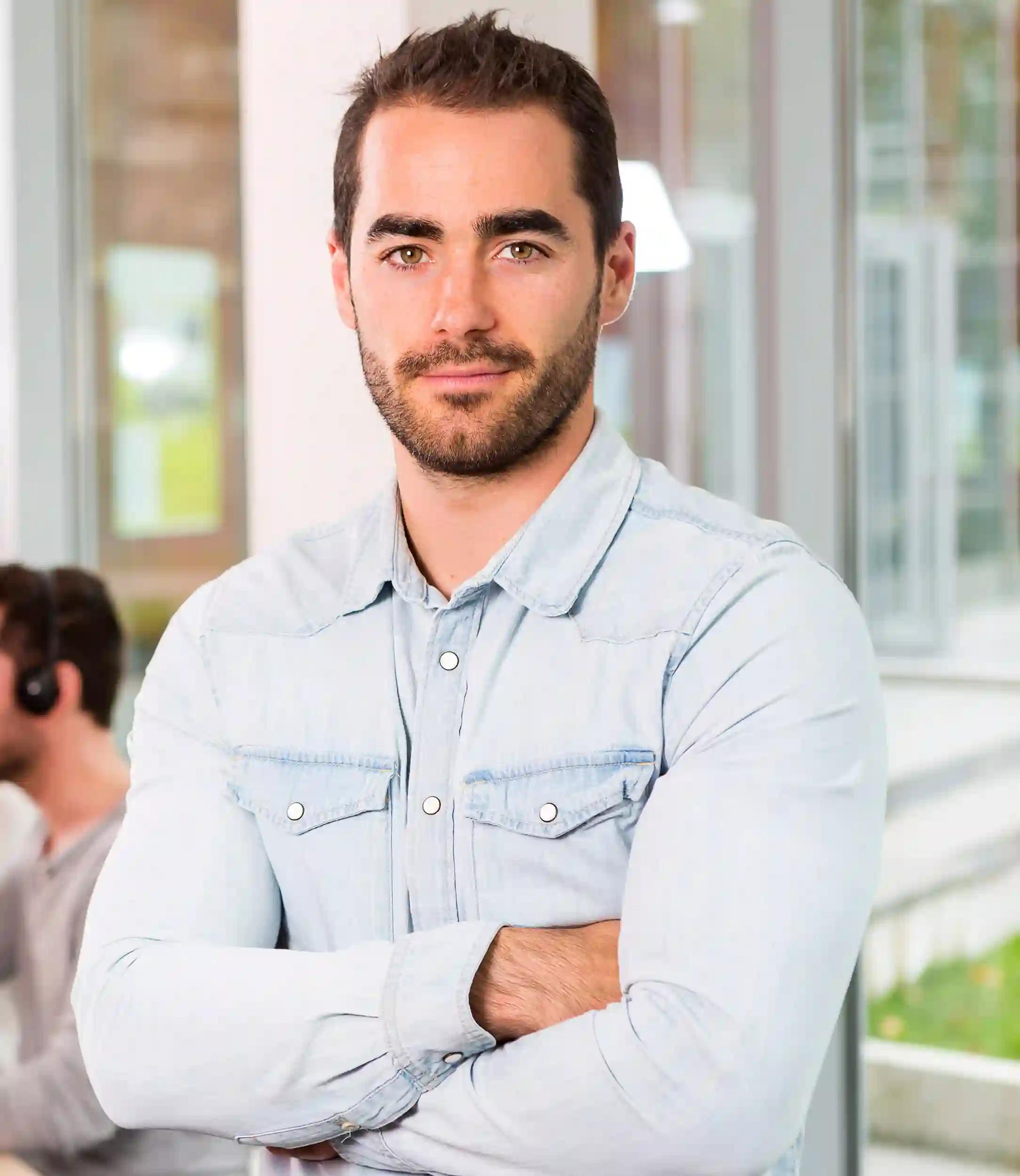 Man standing in an office in front of coworkers who are working by a desk. 